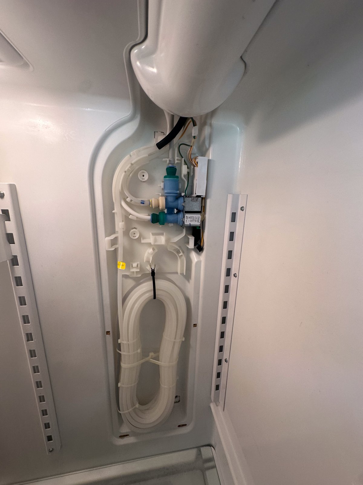 Water inlet valve and supply tubing exposed behind the rear interior panel of a refrigerator during a Dr. Appliance service call